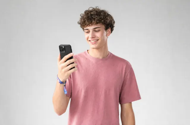 Een jonge man met een festivalbandje om zijn pols kijkt lachend naar zijn telefoon